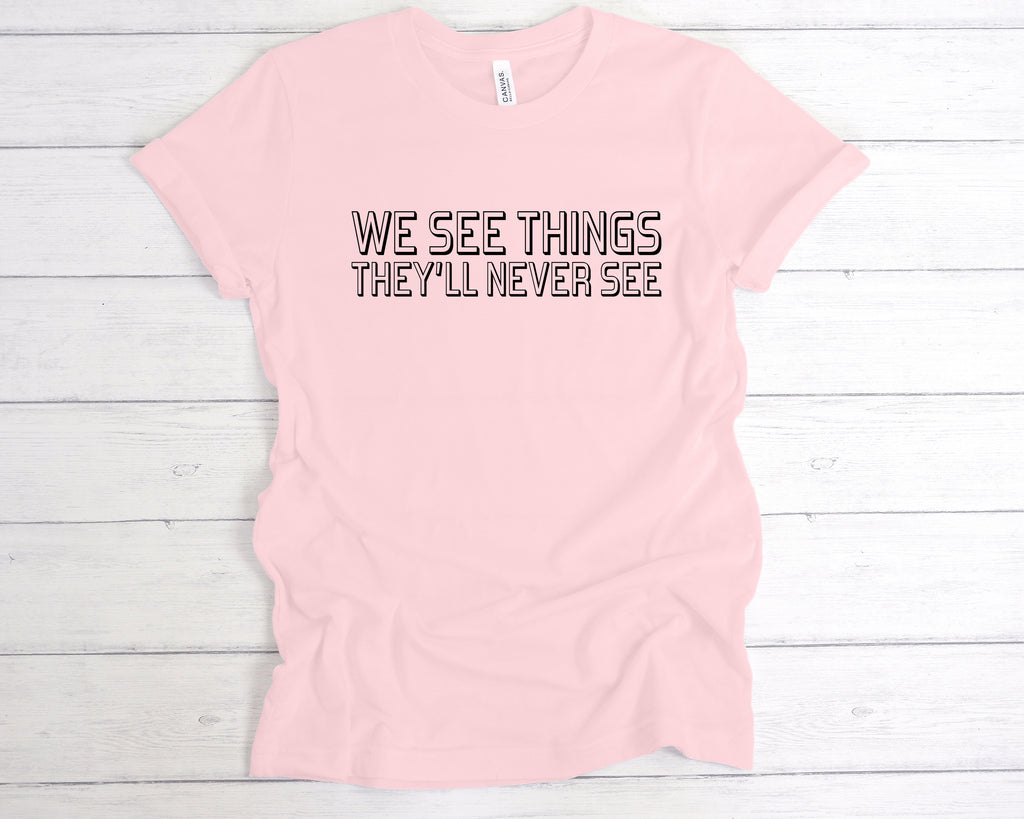 Soft Pink unisex band-style t-shirt featuring the bold slogan "We See Things They’ll Never See" across the chest in a clean, concert-style font. This edgy alternative tee is perfect for music lovers, gig-goers, and fans of underground fashion. Made from soft cotton, it’s ideal for concerts, festivals, or as part of a rock-inspired wardrobe. A great gift for anyone who lives for live music and alternative culture.