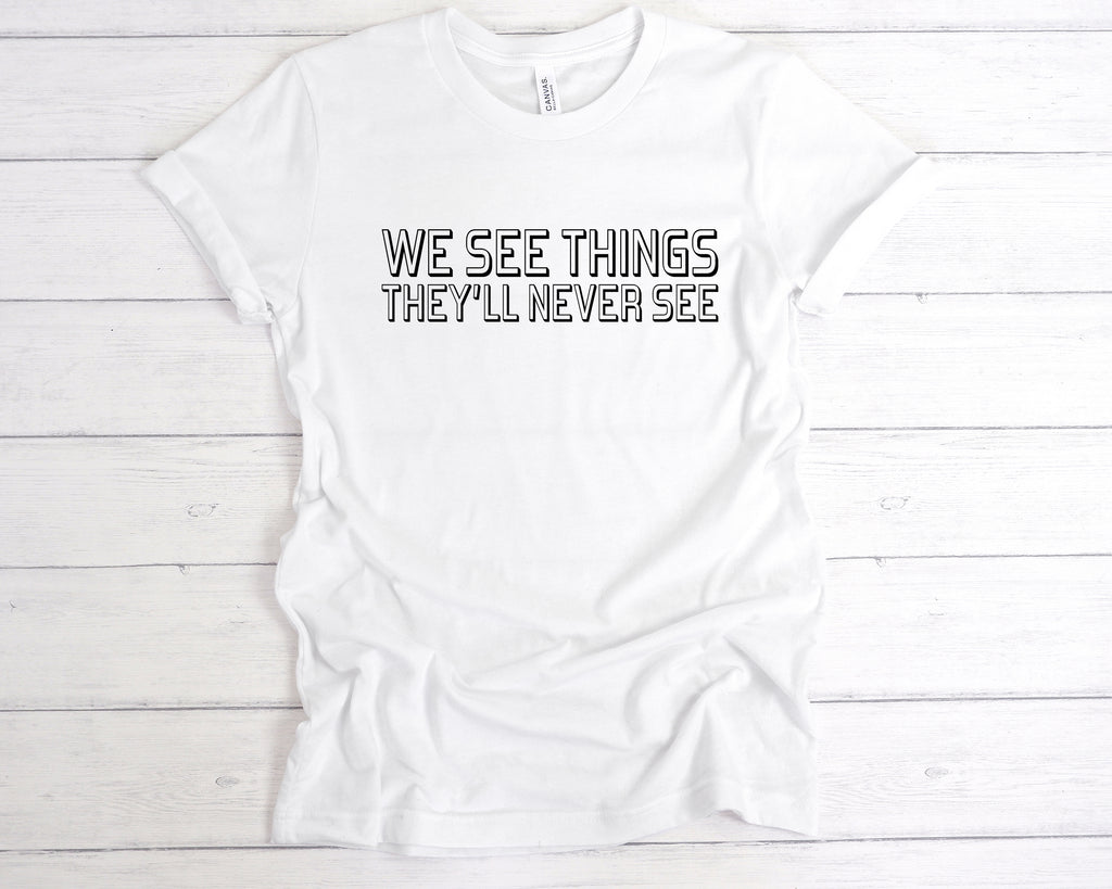 White unisex band-style t-shirt featuring the bold slogan "We See Things They’ll Never See" across the chest in a clean, concert-style font. This edgy alternative tee is perfect for music lovers, gig-goers, and fans of underground fashion. Made from soft cotton, it’s ideal for concerts, festivals, or as part of a rock-inspired wardrobe. A great gift for anyone who lives for live music and alternative culture.